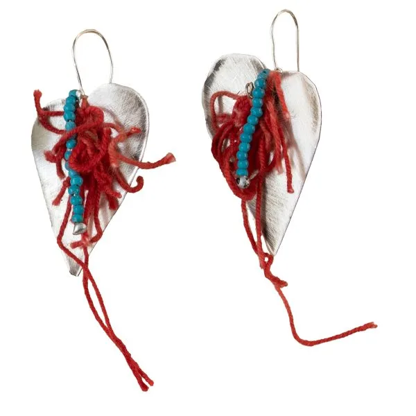 Handmade silver earrings in the shape of a heart, adorned with light blue beads and red woolen threads.