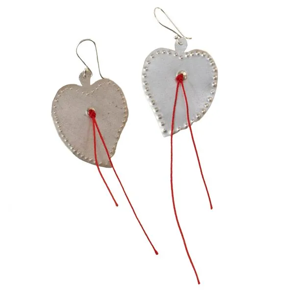 Handmade silver heart-shaped earrings, featuring embossed details along the edges and red threads suspended at the center.